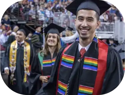 A DU graduate student smiling and walking in a cap and gown during a commencement ceremony.