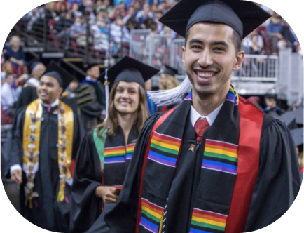 A DU graduate student smiling and walking in a cap and gown during a commencement ceremony.